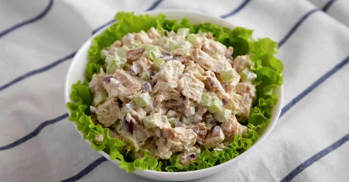 Homemade Chicken Salad Chick Recipe served in a white bowl, garnished with fresh lettuce leaves.