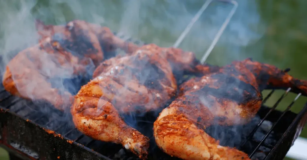 Juicy, spiced chicken legs grilling over an open flame with smoky flavors rising, perfect for preparing tender and flavorful chicken for your grilled chicken wrap recipe.