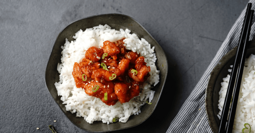 A bowl of rice recipe with Korean chicken, featuring tender chicken in a rich sauce, garnished with sesame seeds and green onions, served over white rice.