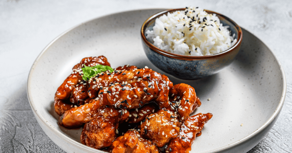 A beautifully presented rice recipe with Korean chicken, featuring tender chicken coated in a rich glaze, garnished with sesame seeds and served with steamed rice in a bowl.
