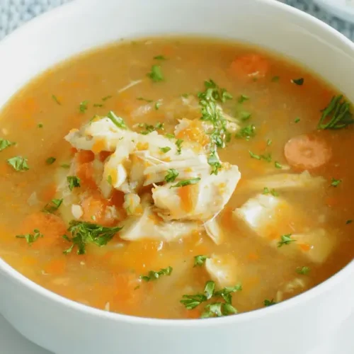 A steaming bowl of Jamaican chicken soup recipe with vegetables, chicken, and aromatic spices.