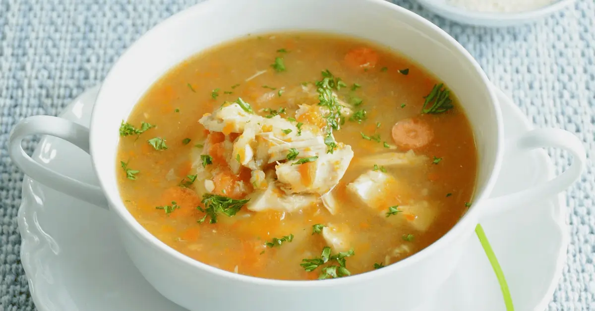 A steaming bowl of Jamaican chicken soup recipe with vegetables, chicken, and aromatic spices.